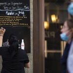 Bares y restaurantes en Madrid. Imagen de una camarera apuntando en una pizarra fuera del local el menú del día.