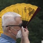 Un hombre con una máscara usa abanico para protegerse mientras espera en la fila de un centro de pruebas de Covid