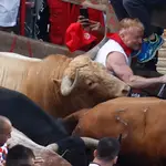 Un mozo es alcanzado por uno de los toros de la ganadería gaditana Núñez del Cuvillo a su llegada a la curva de la calle Estafeta