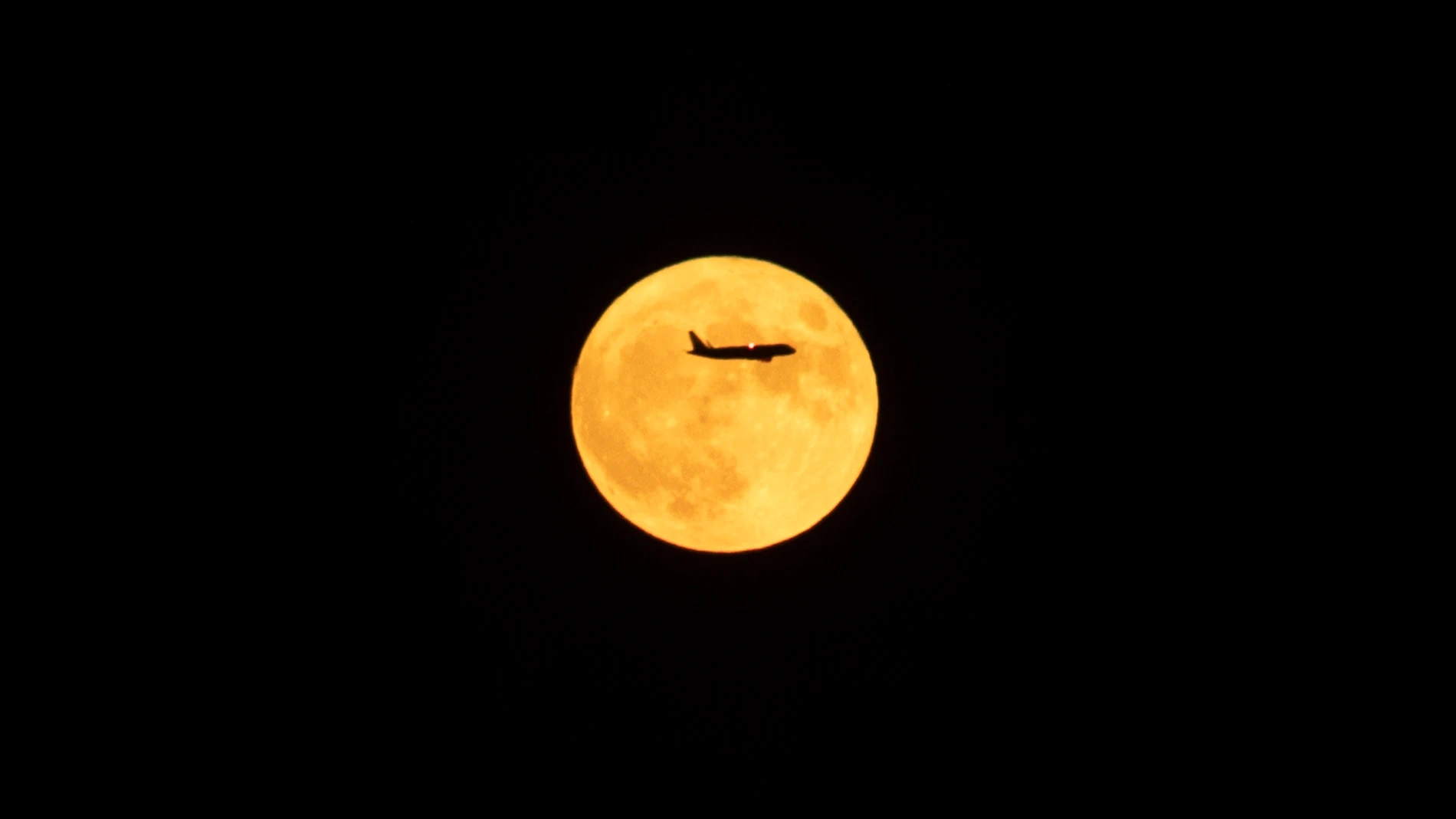 Un avión en dirección al aeropuerto del Prat pasa por delante de la luna llena