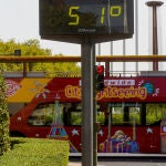 Un autobús turístico pasa sin pasajeros delante de un termómetro que marca 51º en otro día con altas temperaturas en la capital andaluza a 25 de julio del 2022 en Sevilla (Andalucía, España)