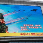 Un hombre (arriba) coloca una cinta a lo largo de un anuncio para conmemorar el 95º aniversario de la fundación del Ejército Popular de Liberación (EPL) expuesto en Pekín