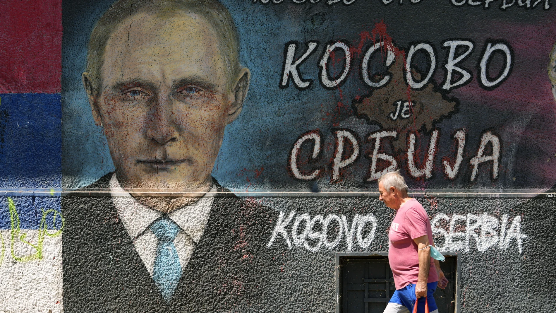 Un hombre pasa junto a un mural de Vladimir Putin en una calle de Belgrado donde se lee «Kosovo es Serbia»
