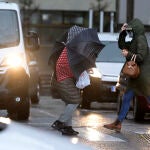 Dos personas cruzan un paso de cebra protegiéndose del mal tiempo