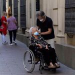 Un hombre ayuda a una mujer en silla de ruedas a colocarse la mascarilla