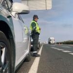 Un agente de la Guardia Civil junto a su coche en una carretera.