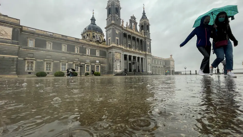 Dos mujeres caminan bajo la lluvia en las inmediaciones de la catedral de la Almudena