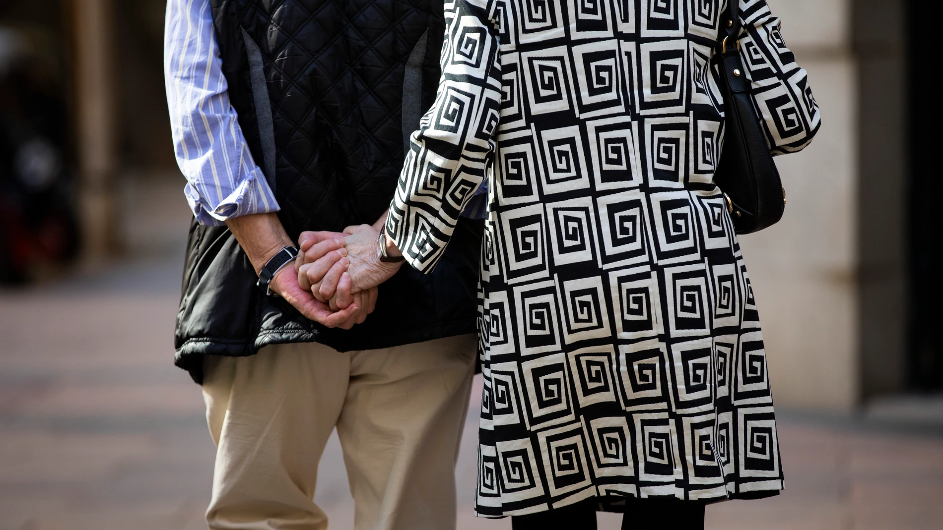 Imagen de una pareja de personas mayores de espaldas cogidos de la mano paseando por Madrid.
