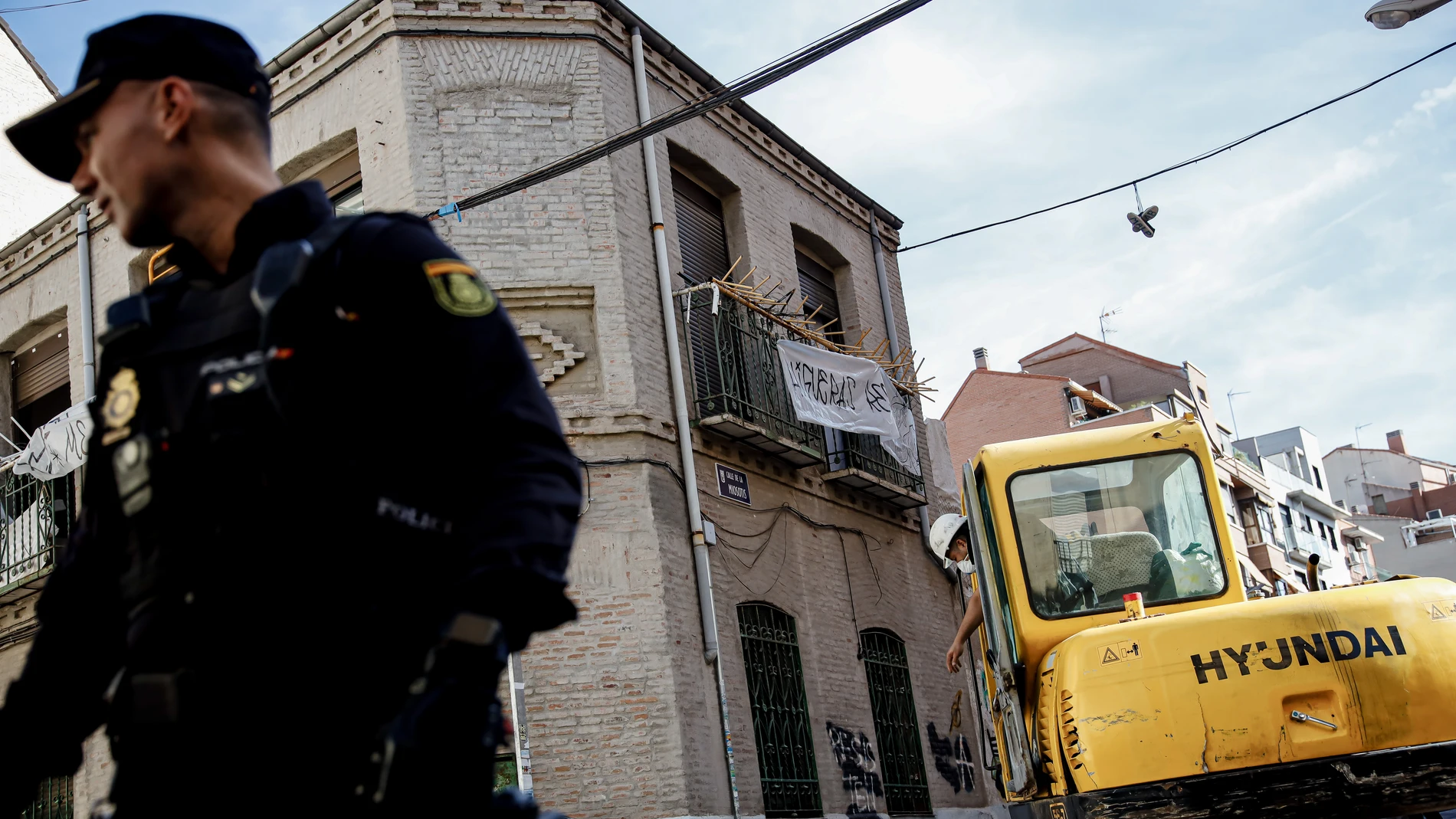 Un agente de Policía Nacional frente a una máquina retroexcavadora durante la demolición del edificio okupado ‘La Higuera’, en el barrio de Tetuán