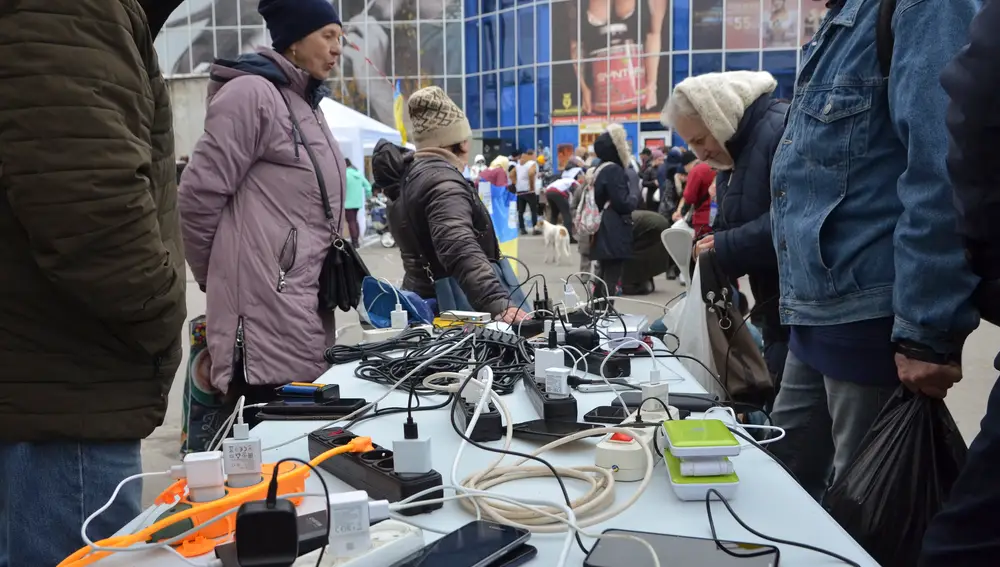 Unos vecinos cargan sus teléfonos móviles con un generador en una calle de la ciudad de Jersón