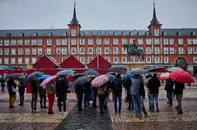 Un grupo de turistas se protegen de la lluvia en la Plaza Mayor de Madrid