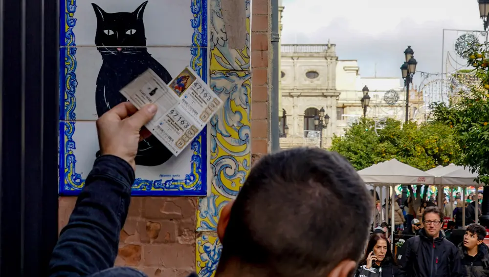 Una persona pone el décimo recién comprado en el azulejo que representa a el gato negro en la administración de loterías ‘El Gato Negro’ situada en la Av de la Constitución. Eduardo Briones / Europa Press