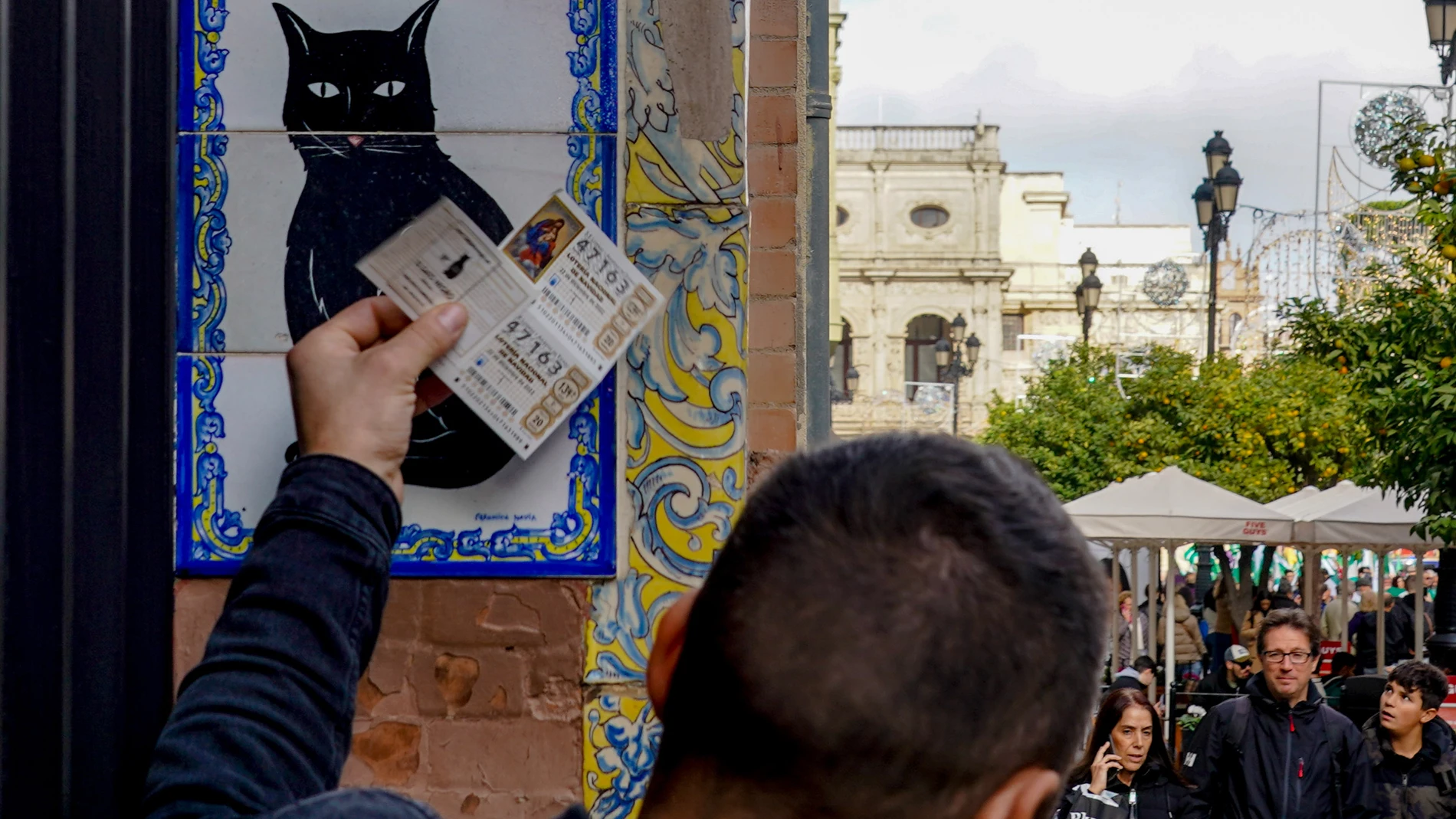 Una persona pone el décimo recién comprado en el azulejo que representa a el gato negro en la administración de loterías ‘El Gato Negro’ situada en la Av de la Constitución. Eduardo Briones / Europa Press