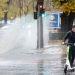 Un hombre usa un patinete eléctrico bajo la lluvia en Madrid