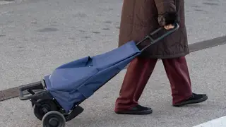 Una mujer mayor sale de un supermercado con un carro de la compra Una mujer mayor sale de un supermercado con un carro de la compra