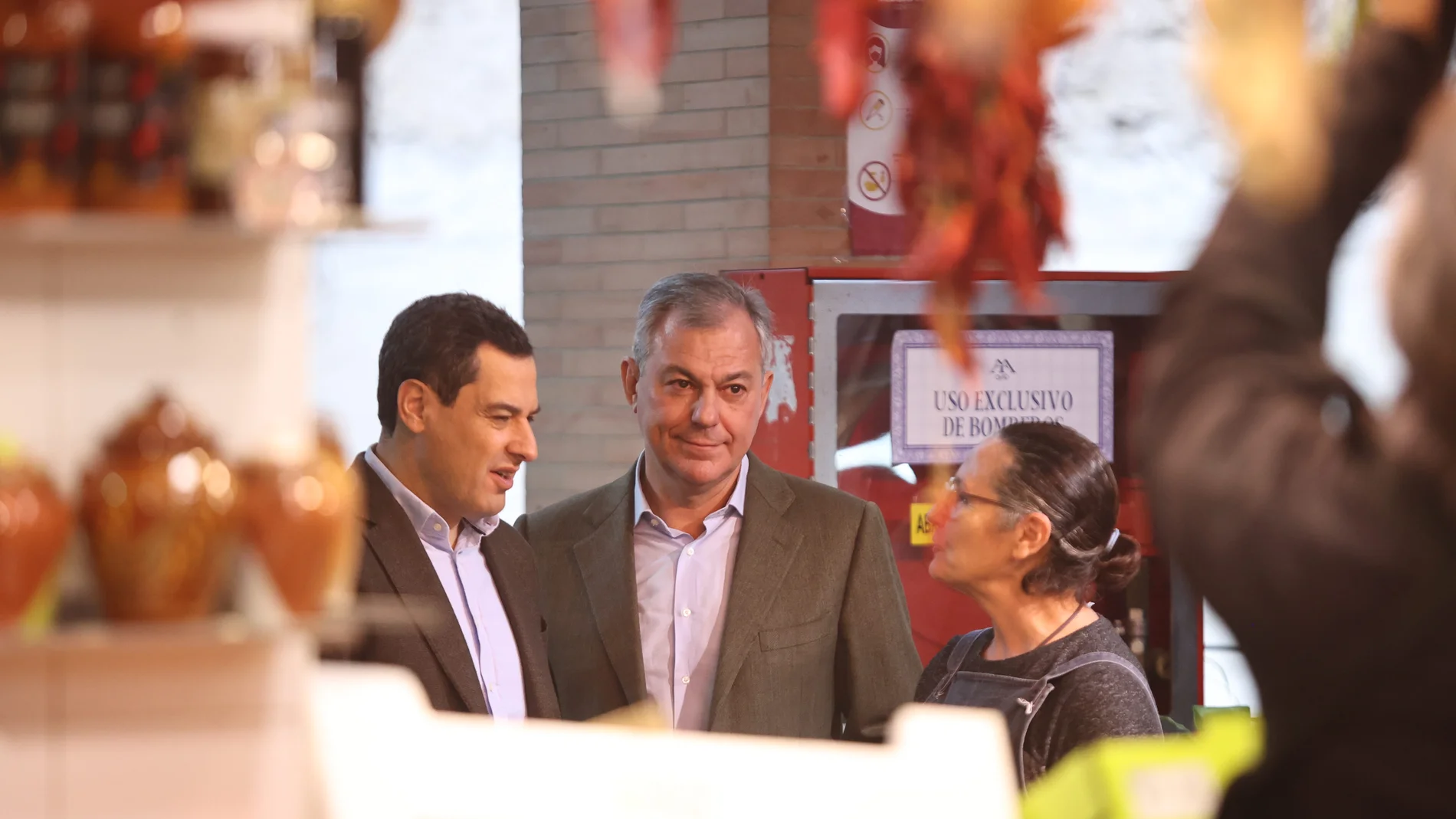 El presidente de la Junta de Andalucía, Juanma Moreno (1i), y el candidato a la alcaldía de Sevilla, José Luis Sanz (2i), dialogan con los vecinos en la plaza de abastos de Triana