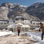 - Varias personas pasan delante del edificio de la antigua estación de tren de Canfranc, cubierta por la nieve acumulada.