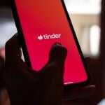 Una mujer joven sostiene un móvil que tiene instalada la aplicación de Tinder