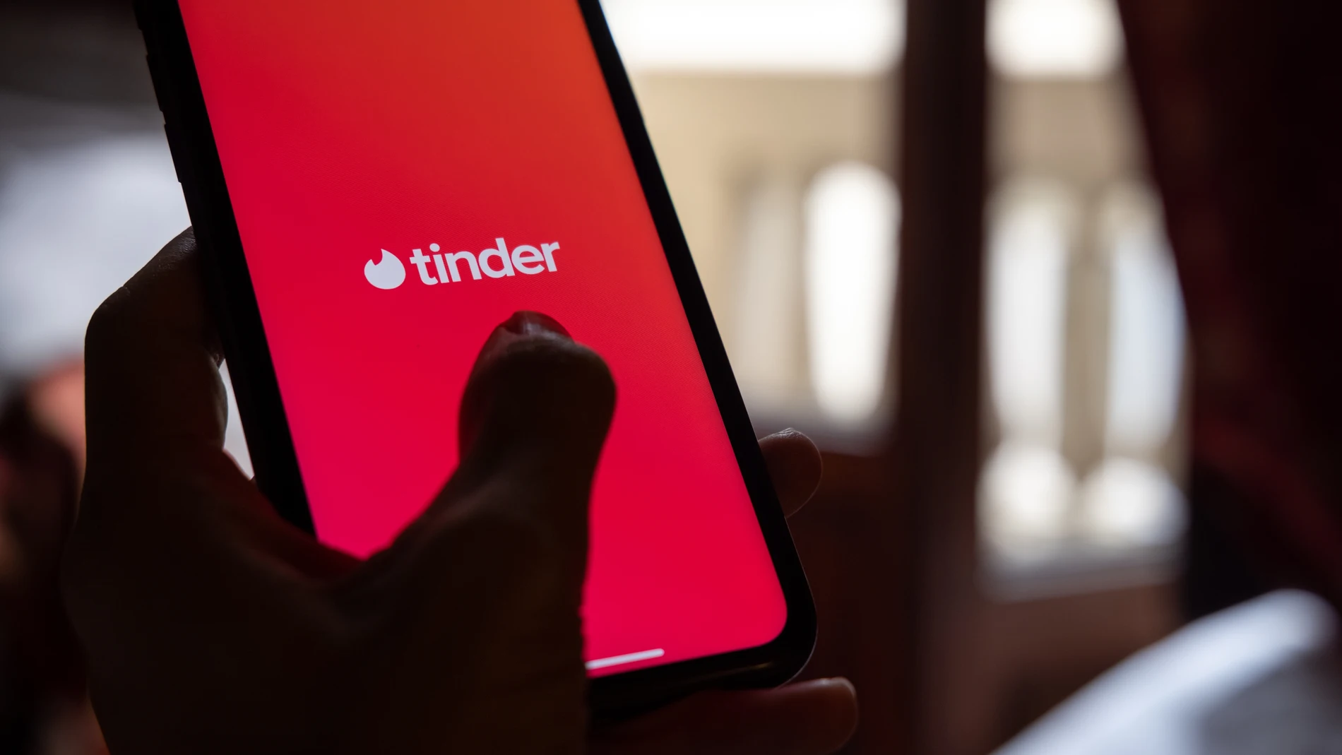 Una mujer joven sostiene un móvil que tiene instalada la aplicación de Tinder