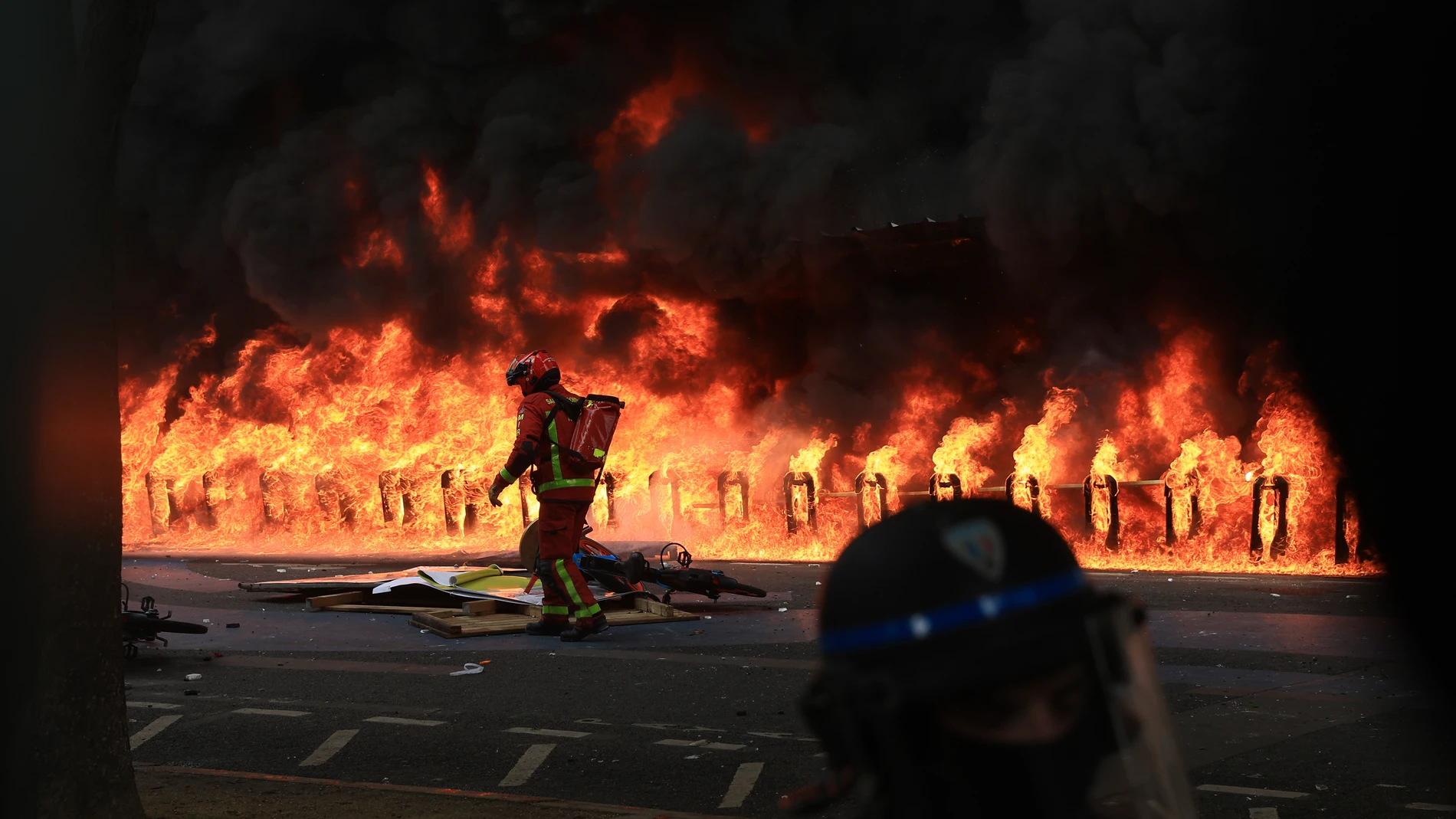 A rescue worker arrives at a fire set in front of a building during a demonstration, Monday, May 1, 2023 in Paris. Across France, thousands marched in what unions hope are the country's biggest May Day demonstrations in years, mobilized against President Emmanuel Macron's recent move to raise the retirement age from 62 to 64. (AP Photo/Aurelien Morissard)