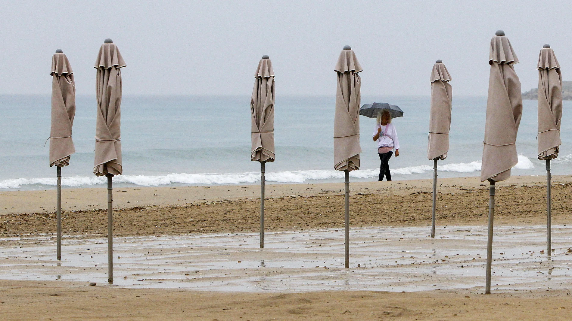 Una persona pasea bajo la lluvia por la playa de El Postiguet de Alicante