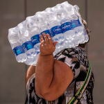 Una mujer lleva botellas de agua en la playa de la Malagueta