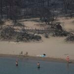 Dos bañistas juegan con una pelota frente a un bosque quemado en una playa cerca de la aldea de Gennadi en Rodas, una turística isla griega en el mar Egeo, al sureste de Grecia, hoy jueves 27 de julio de 2023