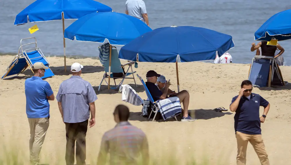 President Joe Biden and first lady Jill Biden sit underneath an umbrella surrounded by Secret Service agents on a beach in Rehoboth Beach, Del., Wednesday, Aug. 2, 2023.