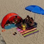 Varias personas se refugian del sol bajo sombrillas en Galicia. 