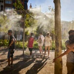 Jóvenes junto a unos aspersores de vapor de agua para intentar refrescarse de la ola de calor por altas temperaturas 