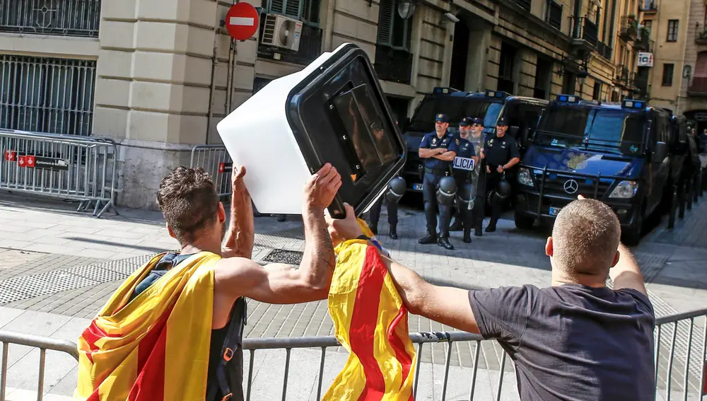 Dos jóvenes muestran una urna empleada el 1-O a los policías nacionales apostados ante la comisaría de la céntrica Via Laietana de Barcelona que permanece cortada por cientos de personas en protesta por la sentencia del procés en la que se condena a los líderes independentistas a penas de entre 9 y 13 años por un delito de sedición.