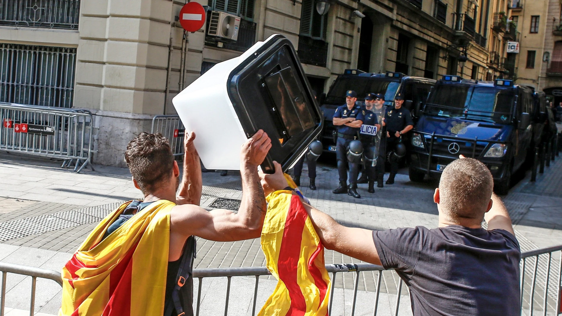 Dos jóvenes muestran una urna empleada el 1-O a los policías nacionales apostados ante la comisaría de la céntrica Via Laietana de Barcelona que permanece cortada por cientos de personas en protesta por la sentencia del procés en la que se condena a los líderes independentistas a penas de entre 9 y 13 años por un delito de sedición.