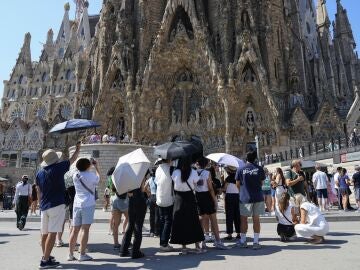 Varios turistas equipados con sombrillas visitan la Sagrada Familia, en Barcelona.
