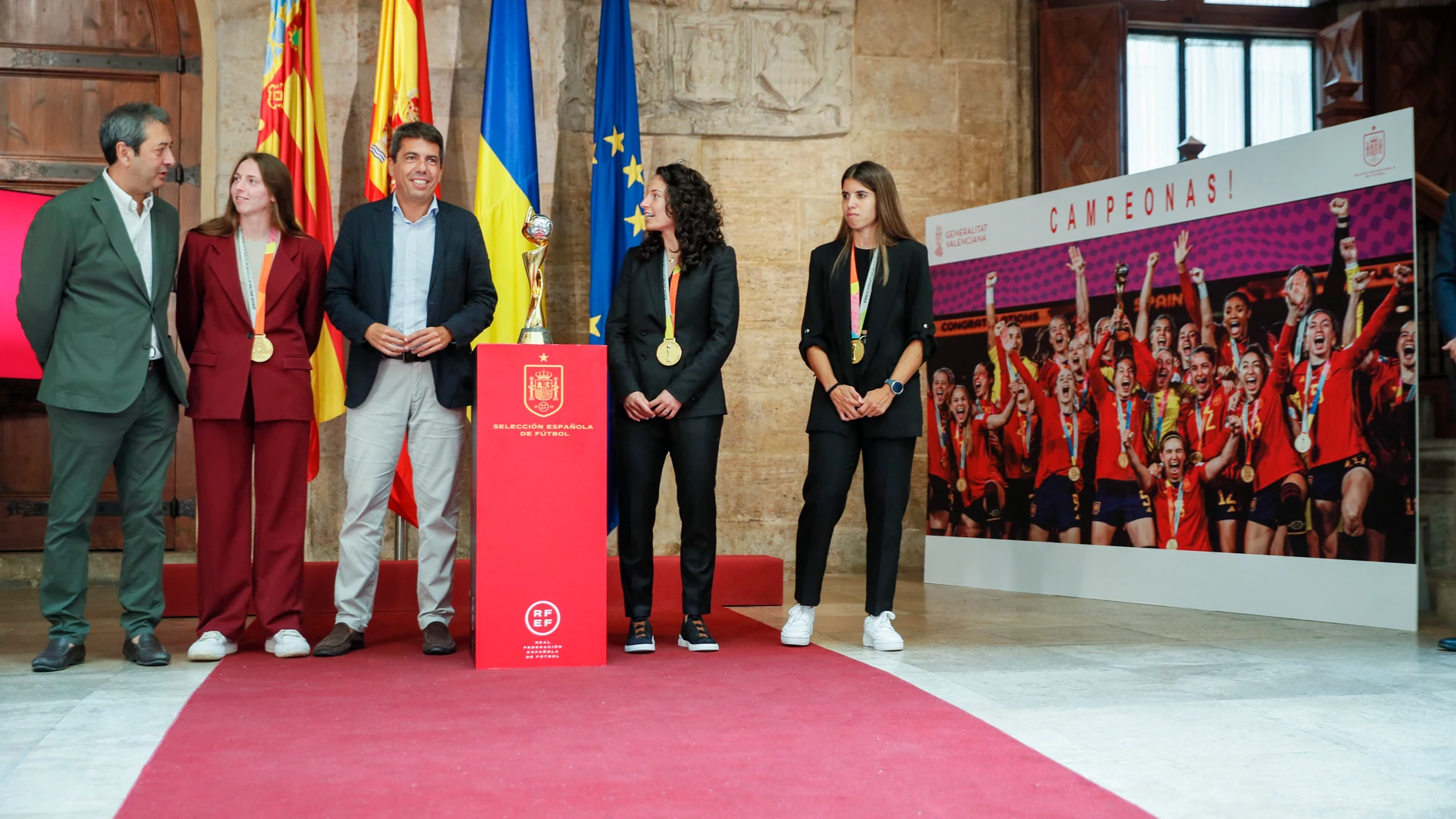 La jugadoras de la selección española de Fútbol, Alba Redondo (d), Ivana Andrés (c) y Enith Salón (i) ,a su llegada al Palau de la Generalitat donde han posado, junto al presidente Mazón (c) y el vicenpresidente Vicente Barrera con la copa de campeonas del Mundo