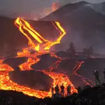 Spanish Army soldiers stand on a hill as lava flows as volcano continues to erupt on the Canary island of La Palma, Spain, Monday, Nov. 29, 2021. Several new volcanic vents opened in La Palma on Sunday, releasing new lava that flowed fast down a ridge and threatened to widen the impact on evacuated land, infrastructure and homes