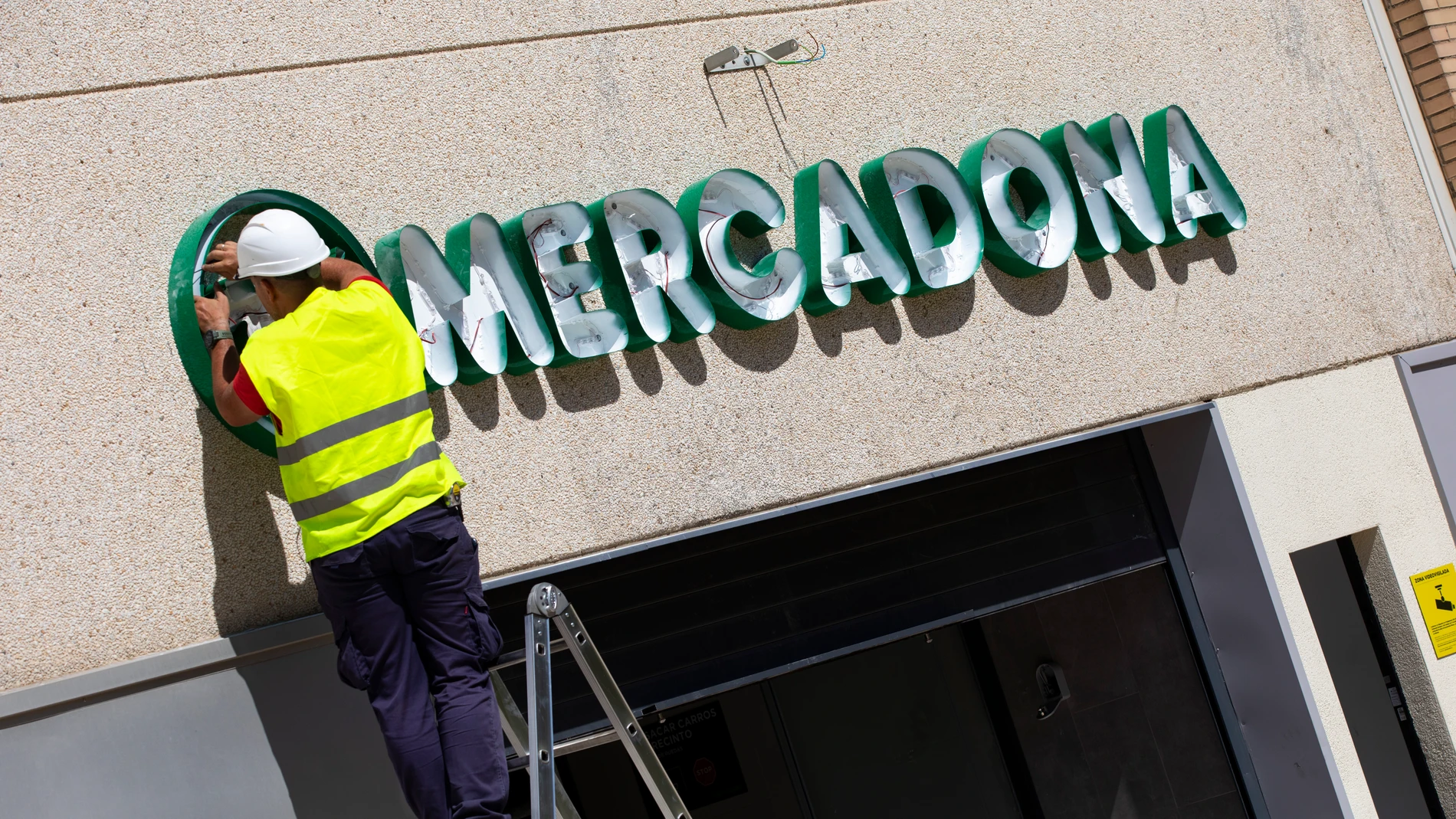 Dos operarios colocan el cartel luminoso de Mercadona en la fachada de una tienda. © Jesús G. Feria.