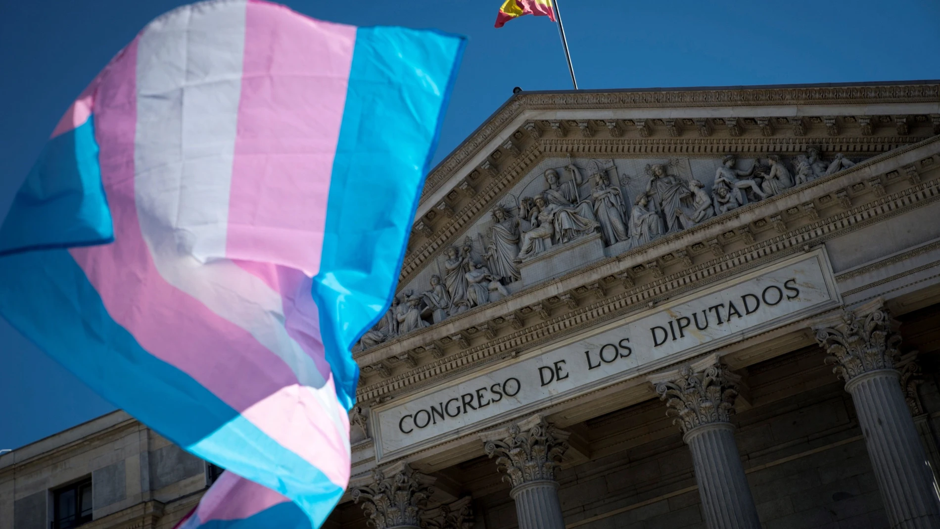 MADRID, 22/06/2020.- Una bandera ondea ante el Congreso de los Diputados mientras representantes de colectivos de personas Trans y de Familias de toda España se manifiestan, este lunes en el centro de Madrid, para mostrar su malestar por el documento interno de PSOE, donde se mostraban contrarios al cumplimiento de su acuerdo programático con respecto a la Ley Trans. EFE/Luca Piergiovanni
