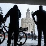 Varias personas se resguardan del viento y la lluvia cerca de la Torre del Oro. Raúl Caro/Efe