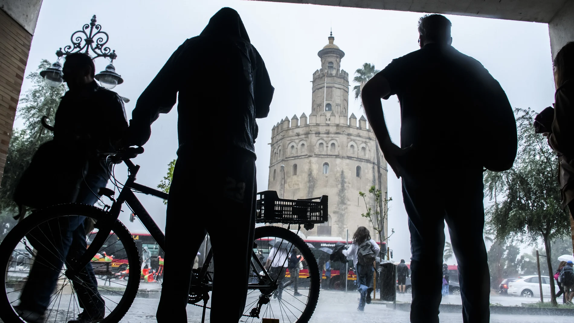 Varias personas se resguardan del viento y la lluvia cerca de la Torre del Oro. Raúl Caro/Efe