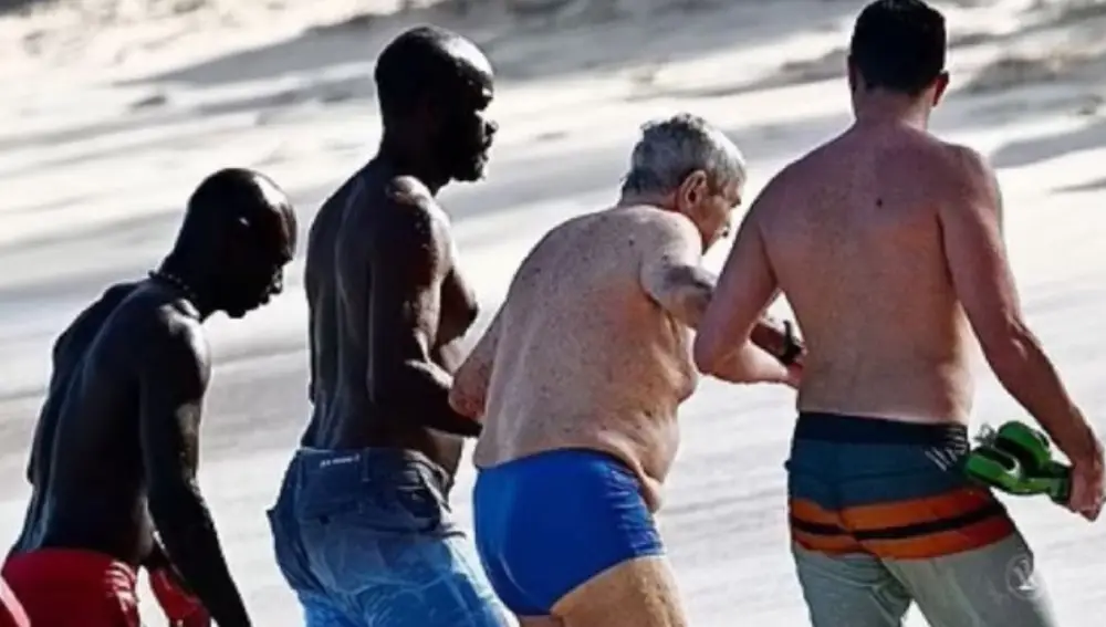 George Soros acompañado de tres hombres que le están ayudando