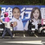 Varias personas pasan junto a un cartel de los candidatos que se presentan a las elecciones presidenciales de Taiwán en Taipéi