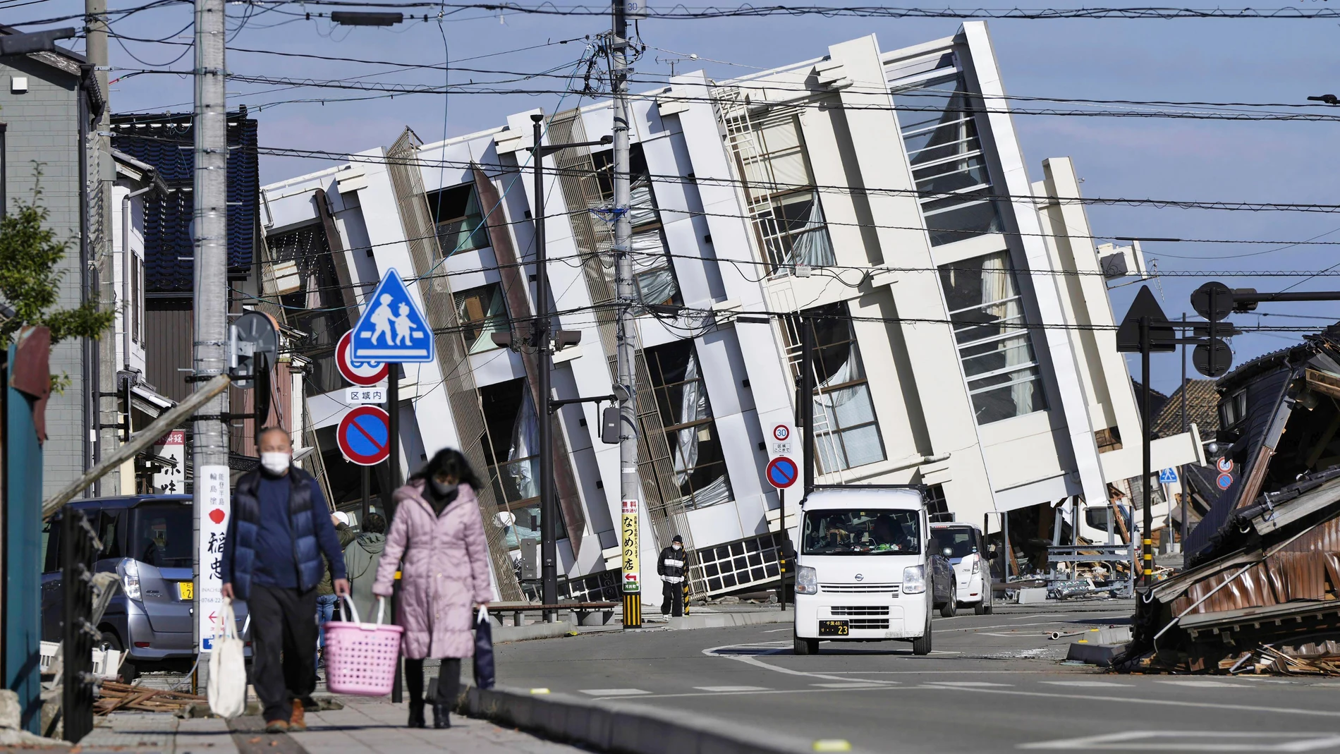 People make their way near a collapsed building due to an earthquake in Wajima, Ishikawa prefecture, Japan Tuesday, Jan. 2, 2024. A series of powerful earthquakes hit western Japan, damaging buildings, vehicles and boats, with officials warning people in some areas on Tuesday to stay away from their homes because of a risk of more strong quakes. (Kyodo News via AP)