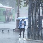 Una mujer camina se cubre de la lluvia con un paragüas