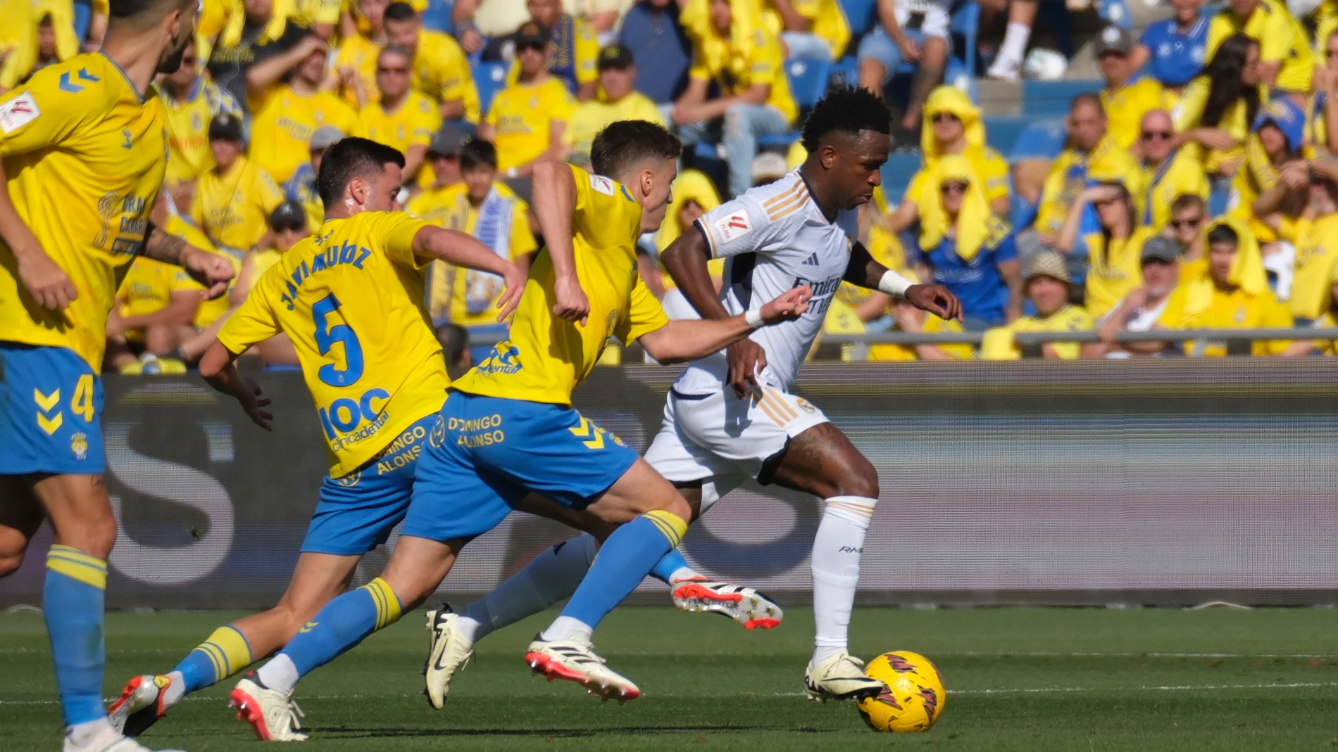 LAS PALMAS DE GRAN CANARIA, 27/01/2024.- El delantero brasileño del Real Madrid Vinicius Jr (d) conduce el balón ante los defensas de Las Palmas Javi Muñoz (i) y Mika Mármol (2d) durante el partido de la jornada 22 de LaLiga EA Sports entre la U.D. Las Palmas y el Real Madrid, este sábado en el estadio de Gran Canaria, en Las Palmas de Gran Canaria. EFE/ Ángel Medina G.