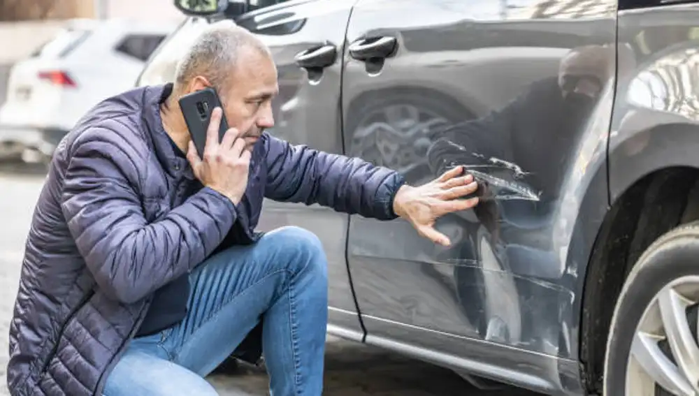 Un hombre observa un rasguño en la carrocería de su coche