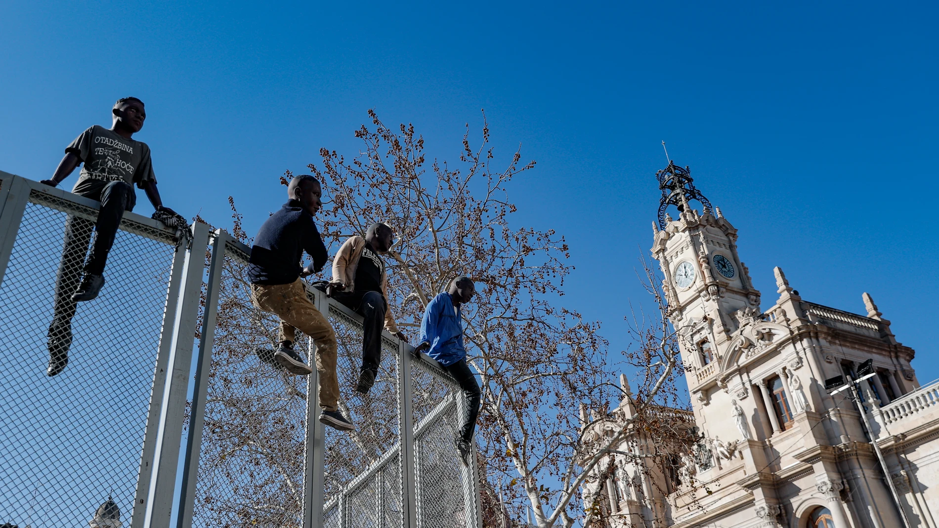 GRAFCVA9169. VALENCIA, 15/03/2024.- Un grupo de cuatro ninots que representan a unos jóvenes tratando de saltar una valla forma parte de la falla de la Plaza del Ayuntamiento que como las cerca de 400 fallas que se planta en Valéncia deberá estar terminada mañana sábado 16 de marzo. EFE/Manuel Bruque