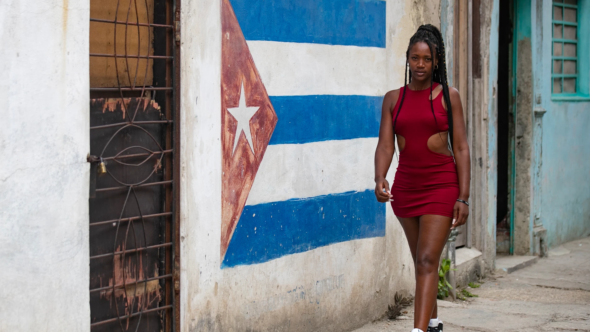 HAB102. LA HABANA (CUBA), 24/03/2024.- Una joven camina frente a una pared pintada con la bandera cubana este domingo en La Habana (Cuba). EFE/ Yander Zamora
