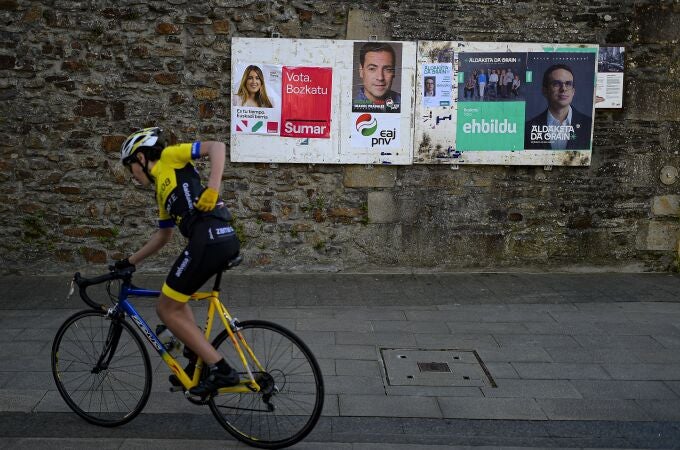 A cyclist passes electoral posters with candidates Pello Otxandiano for EH Bildu, a coalition of pro-independence and nationalist Basque parties, right, Imanol Pradales fo PNV (Basque nationalist party) and Alba Garcia for Sumar, left, in Otxandio, northern Spain.