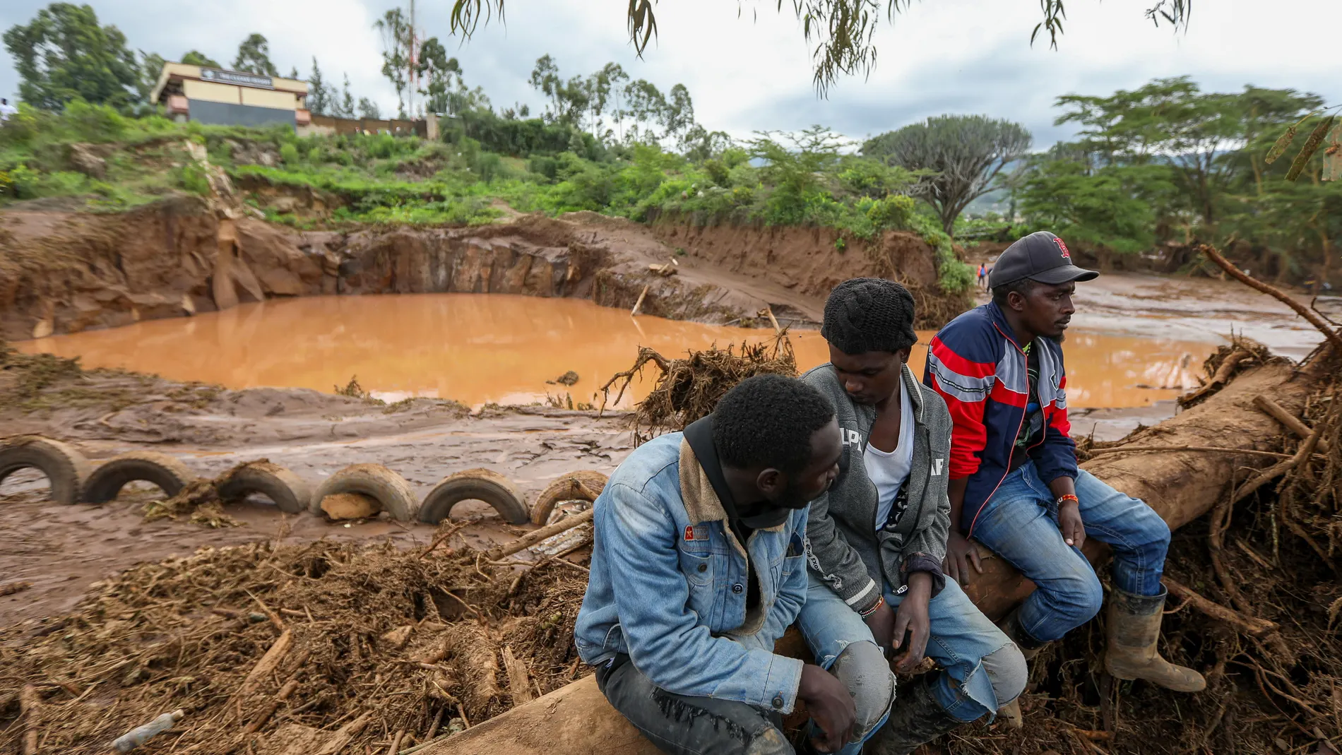 Mai Mahiu (Kenya), 29/04/2024.- A group of men sit on a tree next to an area flooded after Old Kijabe Dam burst its banks and caused flash floods through several villages in Mai Mahiu, in the Rift Valley region of Naivasha, Kenya, 29 April 2024. The flash floods left behind a trail of damaged houses that got swept away, claiming 42 death so far as search and rescue mission continues, according to Kenya Red Cross Society. Kenya and the wider East African region continue to experience flooding ...