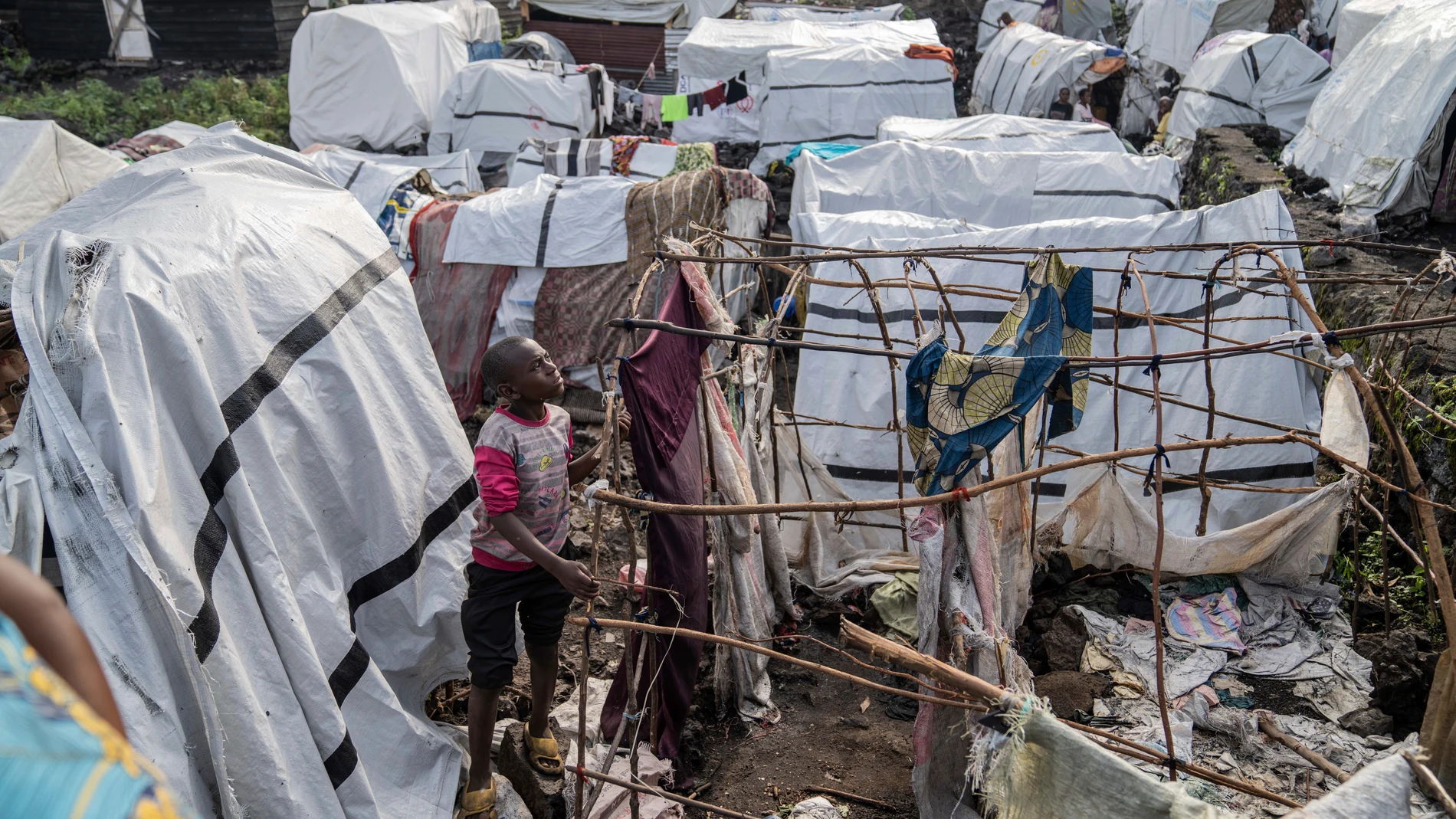 People gather at the side of an explosion in a refugee camp on the outskirts of Goma, Democratic Republic of the Congo, Friday, May, 3, 2024. The Congolese army says a bomb at a refugee camp in eastern Congo has killed at least 5 people, including children. An army spokesman blamed the attack at the Mugunga refugee camp in North Kivu on a rebel group, known as M23, with alleged links to Rwanda, in a statement provided to The Associated Press. (AP Photo/Moses Sawasawa)